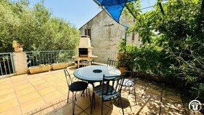 Une terrasse avec une table ronde et des chaises, un barbecue et des plantes en pot.