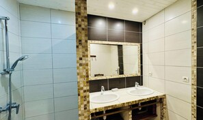 Een badkamer met twee wasbakken, een douche en een spiegel.