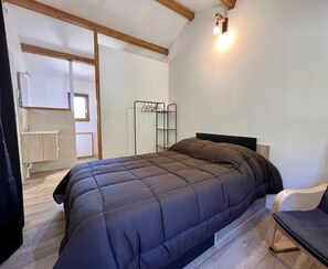 Un dormitorio con cama, una silla, un armario y una lámpara fijada a la pared.