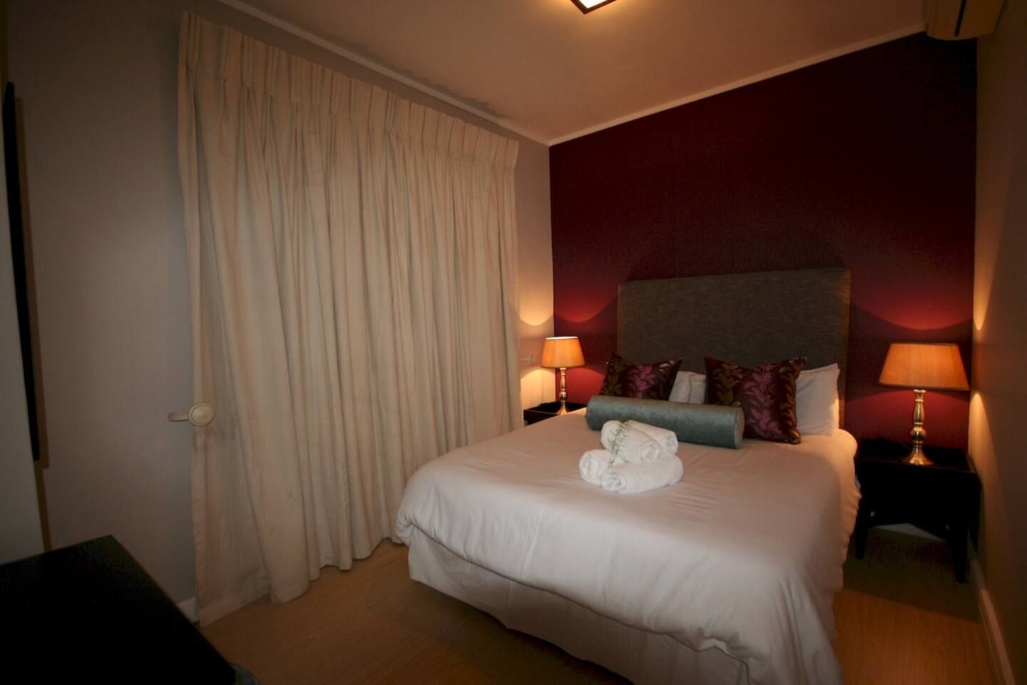 Una habitación de hotel con una cama grande, dos lámparas de noche, un cabecero y una cortina.