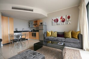 A modern living room with a grey sofa, a coffee table, and a dining area with chairs and a kitchen in the background.