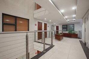 A modern hotel lobby with a reception desk, a staircase, and a plant.