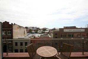 Een balkon met een tafel en twee stoelen, met uitzicht op een stadslandschap met gebouwen en een heldere lucht.