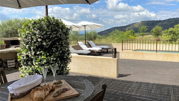 Una terrazza esterna con tavolo in legno apparecchiato per un pasto, poltrone relax e vista sulla campagna.