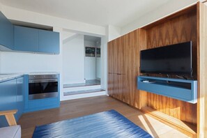 A modern kitchen with blue cabinetry, a built-in oven, and a flat-screen TV mounted on a wooden wall.