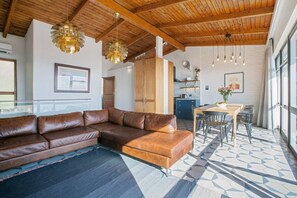 A modern living room with a leather sectional sofa, a dining area with a wooden table and chairs, and a kitchen in the background.