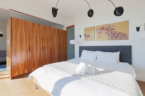 A bedroom with a large bed, a wooden wardrobe, and artwork on the wall.