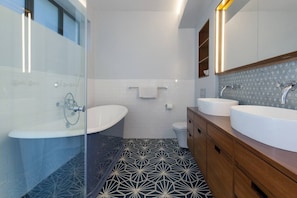 Un bagno moderno con box doccia in vetro, una vasca da bagno freestanding, un water e un mobile lavabo con due lavandini.