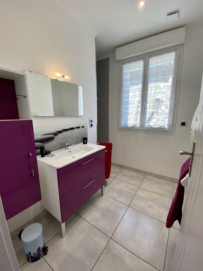 Un bany modern amb un rentapeus blanc, mobles de color morat i una finestra amb vidre mat.