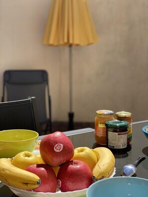 A table with a bowl of fruits, including apples and bananas, and two jars of preserves. - Le Patio - ROQUEFORT DES CORBIERES (ROQUEFORT DES CORBIERES)