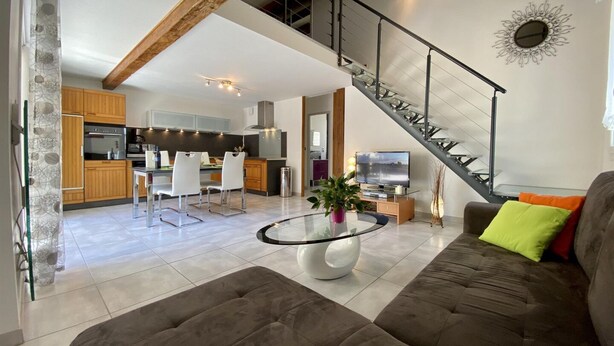 Ein modernes Wohnzimmer mit einem braunen Sofa, einem Glastisch und einer Treppe, die in eine obere Etage führt.