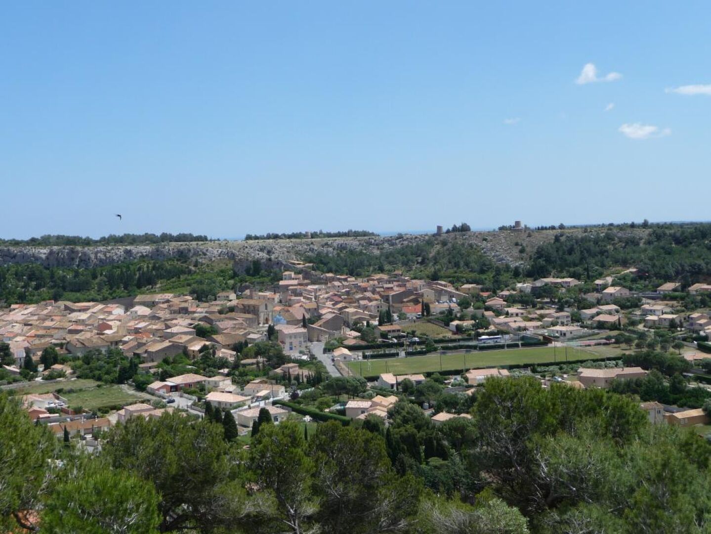 A coastal town with a mix of residential buildings and open spaces, a clear sky, and a distant hill with a structure on top.