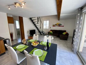 Ein Essbereich mit einem Tisch für zwei Personen, eine Treppe und ein Wohnzimmer mit einer Couch und einem Gemälde.
