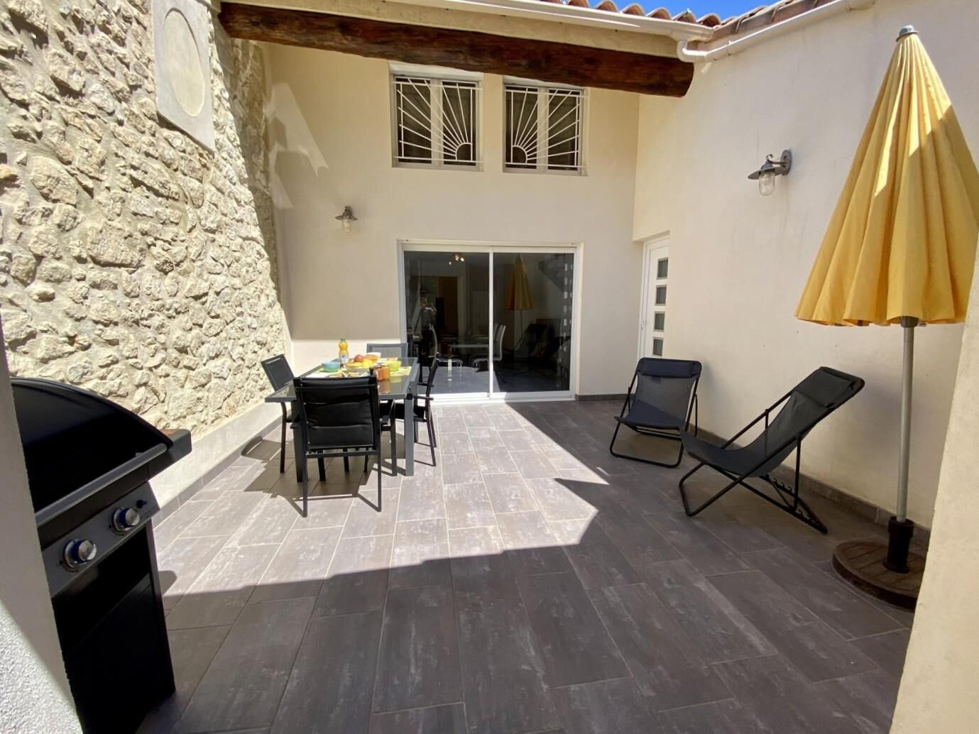 Un patio con mesa, sillas, una parrilla y un paraguas amarillo.