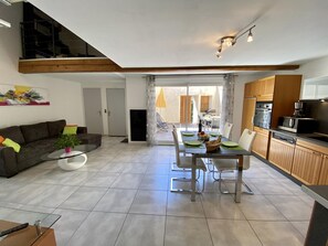 A modern living room with a dining area, kitchen, and a staircase leading to an upper level. - Le Patio - ROQUEFORT DES CORBIERES (ROQUEFORT DES CORBIERES)