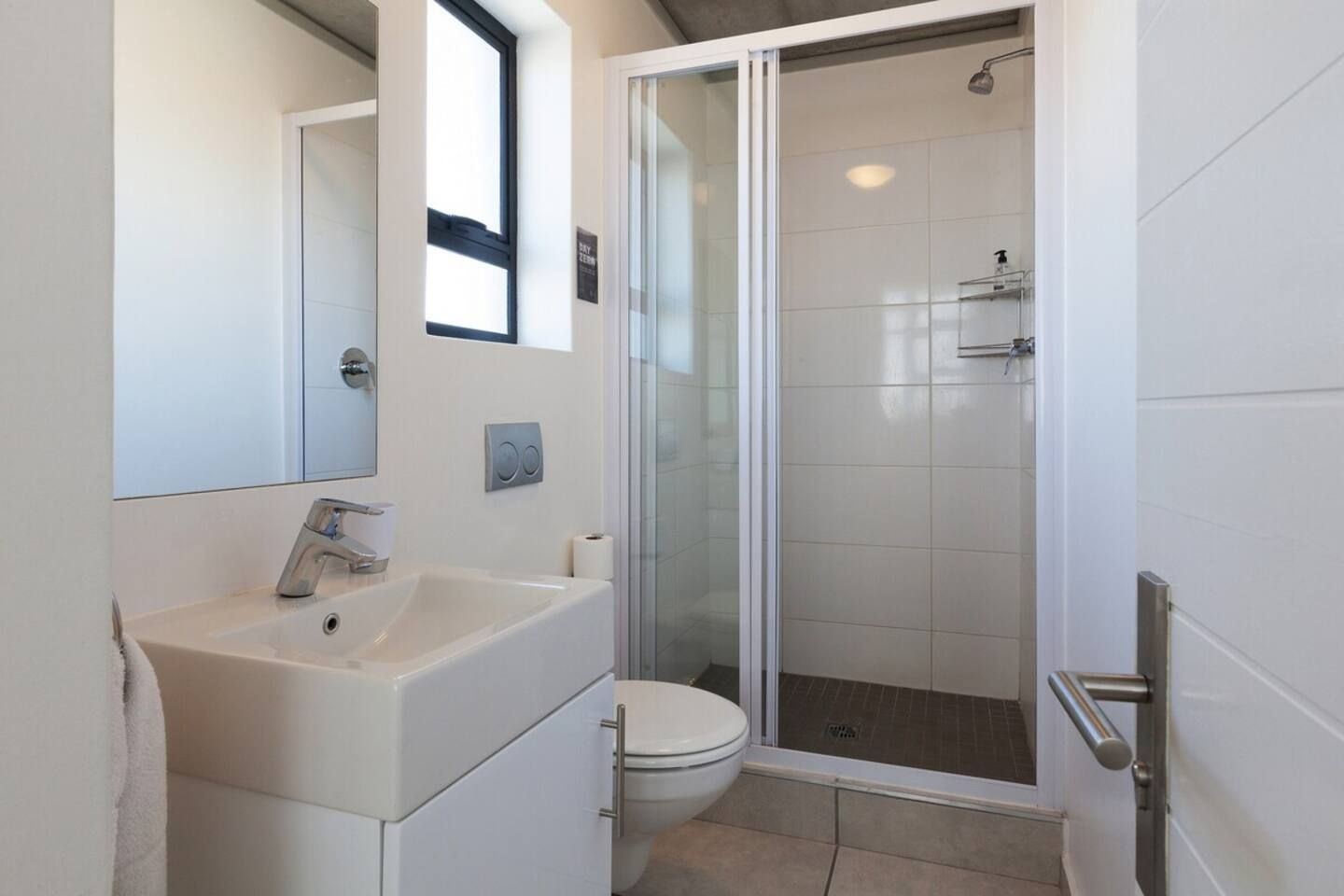 Uma casa de banho moderna com cabine de duche em vidro, uma sanita e uma pia branca.
