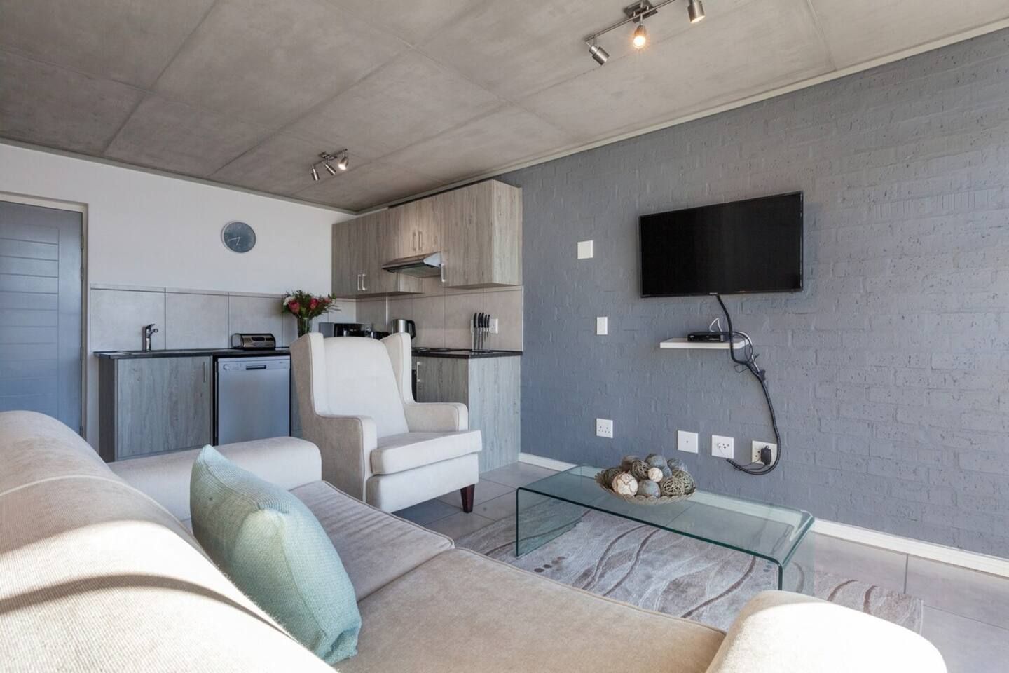 A modern living room with a sofa, a glass coffee table, and a flat-screen TV mounted on the wall.