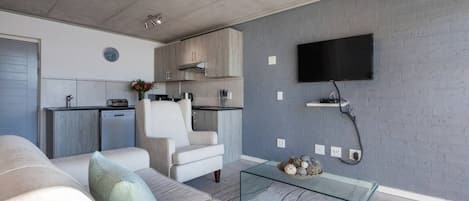 A modern living room with a sofa, a glass coffee table, and a flat-screen TV mounted on the wall.