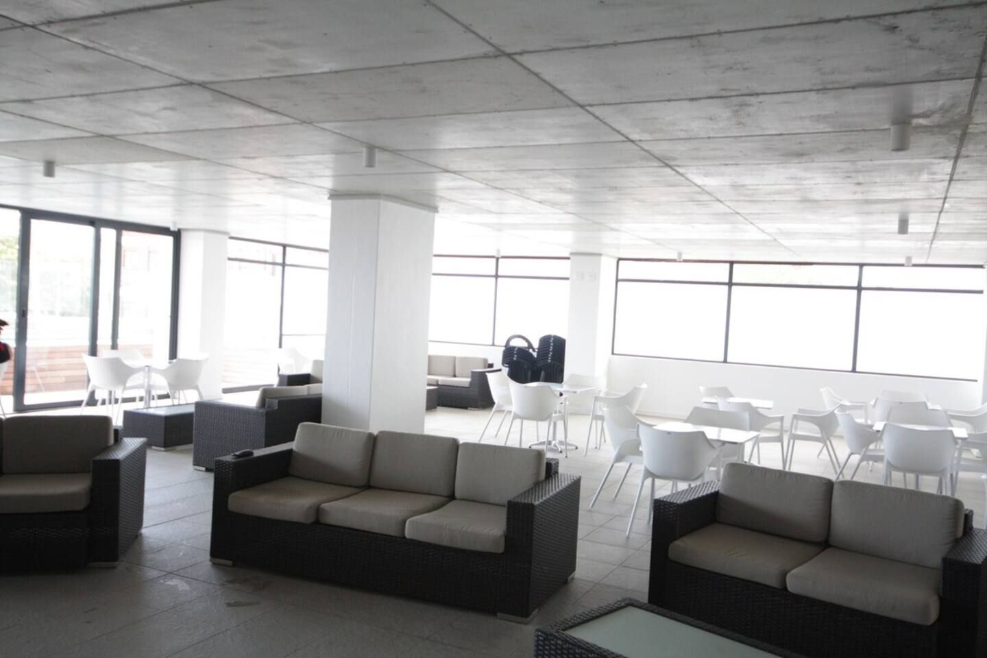 Un espacio interior amplio con arreglos de asientos, ventanas grandes y un techo alto.