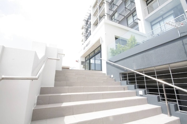A set of outdoor stairs leading to a building with a modern design, featuring a metal handrail and a glass facade.