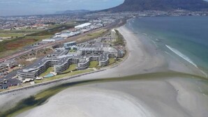 A coastal hotel with a beachfront view, a parking lot, and a prominent mountain in the background. - Key West 417 by Ctha (Milnerton)