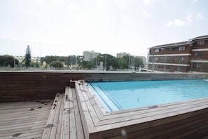 A rooftop swimming pool with wooden deck and a view of surrounding buildings.