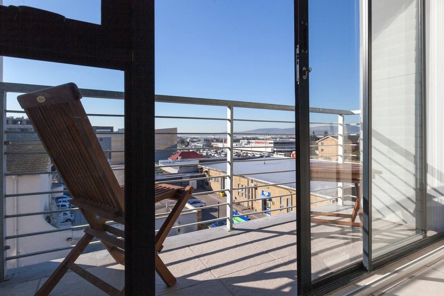 A balcony with a wooden chair, a glass door, and a view of a parking lot and buildings.