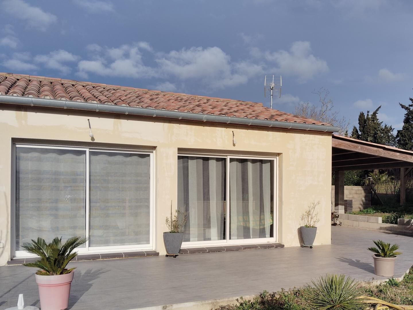 Une maison moderne dotée de grandes portes-fenêtres coulissantes, d’un toit en tuiles et d’une antenne parabolique.