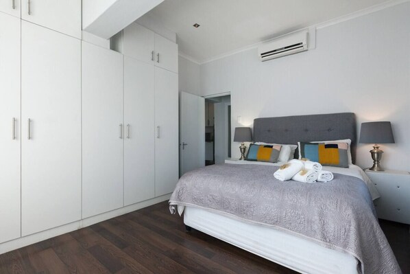 Une chambre à coucher comprenant un lit, des lampes de chevet, une armoire et une porte donnant sur une autre pièce.