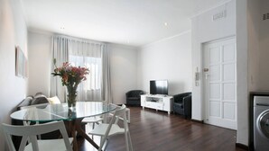 Una sala de estar moderna con una mesa de comedor de vidrio, sillas blancas, un sofá, un mueble para televisor y una lavadora.