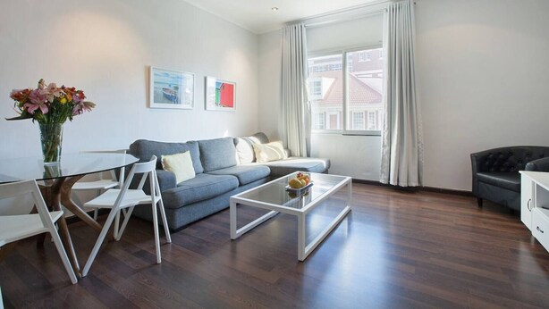 Una sala de estar moderna con una mesa de centro de vidrio, un sofá gris y una mesa de comedor con sillas.