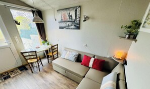 Una sala acogedora con un sofá, una mesa de comedor y sillas. Hay un cuadro en la pared y una planta en un estante.