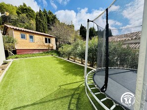 Un patio trasero con un trampolín, una casita de madera y un césped bien cuidado.