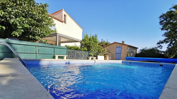 A swimming pool with clear blue water, surrounded by a tiled deck and a green fence. - La barnede - BAGES - Gîte (BAGES)