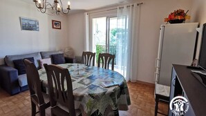 A dining area with a round table, chairs, a chandelier, a sofa, a fan, and a refrigerator. - La barnede - BAGES - Gîte (BAGES)