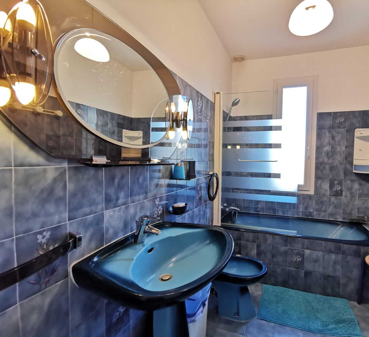 A modern bathroom with a large mirror, two sinks, a toilet, and a shower.