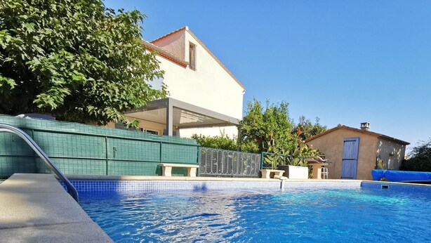 A swimming pool with clear blue water, surrounded by a tiled deck and a green fence.