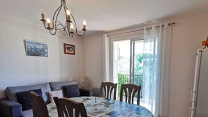 A dining area with a round table, chairs, a chandelier, a sofa, a fan, and a refrigerator.