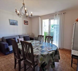 Un comedor con una mesa redonda, sillas, una araña, un sofá, un ventilador y un refrigerador.