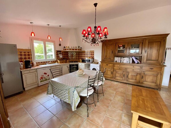 A kitchen with a dining table, chairs, a chandelier, and wooden cabinets. - Petite Pinède - CANET D'AUDE (CANET D'AUDE)
