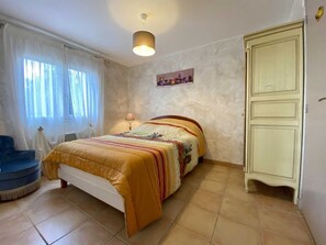 Quarto com cama, poltrona, guarda-roupa e janela com cortinas.