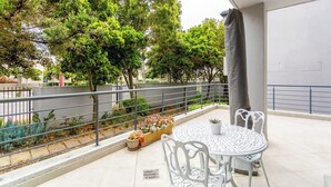Un patio exterior con una mesa redonda y sillas, rodeado por una barandilla metálica y macetas con plantas.