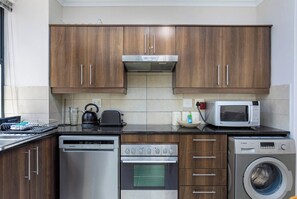 A modern kitchen with wooden cabinets, a stainless steel dishwasher, an oven, a microwave, and a washing machine.
