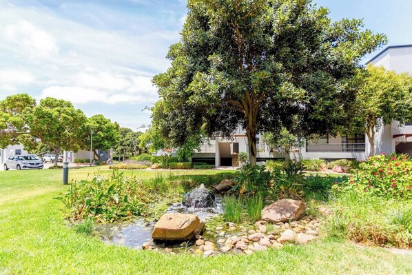 Un jardín ajardinado con un estanque, rocas y un árbol.