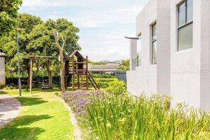 A playground with climbing structures and a garden with flowers.