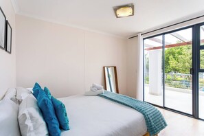 Un dormitorio con cama, un ventanal y vistas al exterior con vegetación.