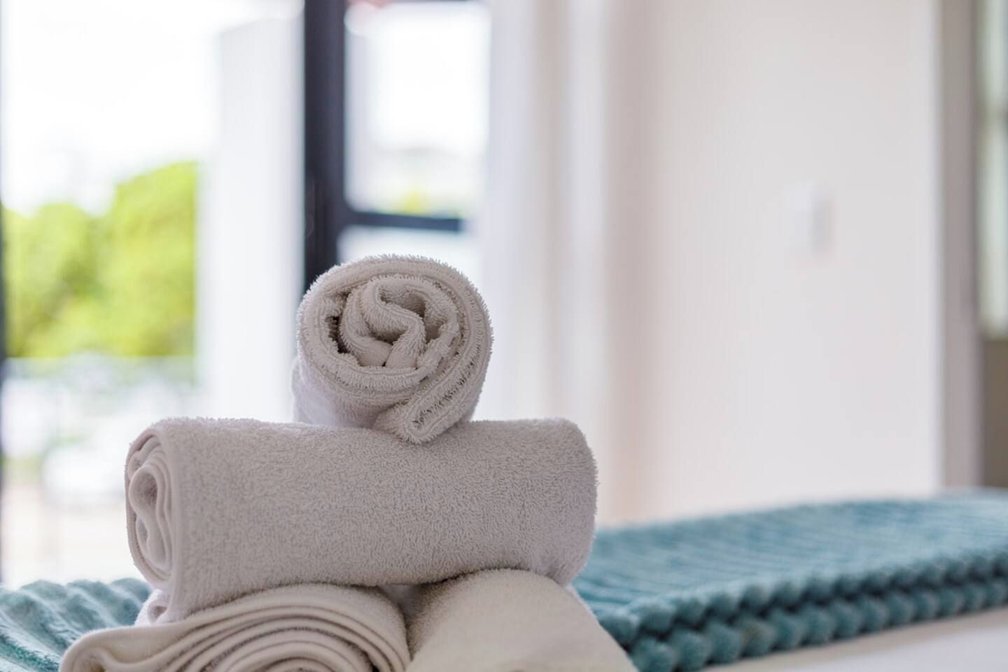 Un mucchio di asciugamani ordinatamente piegati su un letto con una coperta blu.
