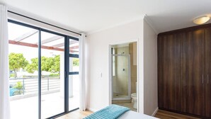 Un dormitorio con un amplio ventanal corredero, un armario de madera y zona de ducha.