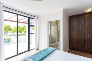Una camera da letto con un'ampia porta finestra, un armadio in legno e un angolo doccia.