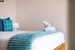 A neatly made bed with a white comforter and a teal throw blanket.